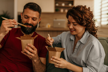 Obraz premium Couple sharing takeaway noodles with chopsticks at home