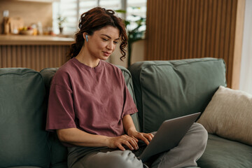 Obraz premium Woman working remotely from home using laptop and earbuds