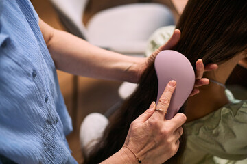 Close up of woman brushing girl hair, detangling long strands during home grooming routine. Suitable for parenting, haircare, hygiene, self care, or family lifestyle marketing