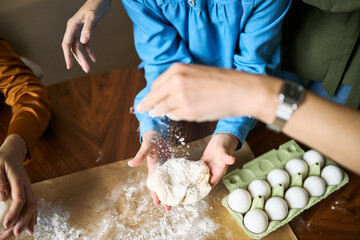 Overhead shot of family hands preparing dough and sprinkling flour beside eggs during home baking....