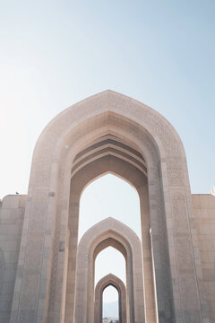 View of the repetitive stone arches with intricate carvings at the Sultan Qaboos Grand Mosque and a small bird perched on a ledge in Oman.