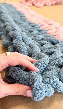 Hand holding chunky knit blanket on craft workspace surface