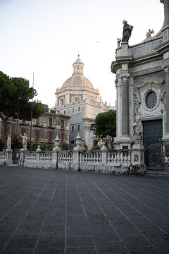 View of the ornate baroque architecture and statues of the Catania Cathedral with the dome of Badia di Sant'Agata in Catania, Sicily, Italy.