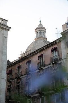 View of a historic building with balconies and red awnings featuring a large dome in the background Catania, Sicily, Italy.