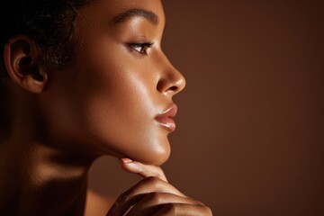 Fototapeta premium Close-up profile image of a confident Black woman, glowing skin and polished nails in a rich brown backdrop