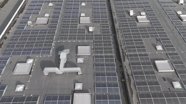 Genk, Belgium. Aerial drone glide over industrial rooftop covered with solar panels showcasing renewable energy infrastructure. Forward drone flight.