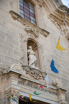 View of the ornate facade and statue of Saint Bartholomew on the Cathedral of St. Bartholomew with colorful festive flags Lipari, Sicily, Italy.