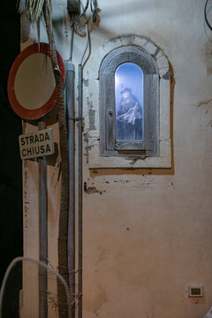 View of a small religious shrine with an illuminated statue of the Virgin Mary set into an old wall next to a road closed sign at night in Lipari, Sicily, Italy.