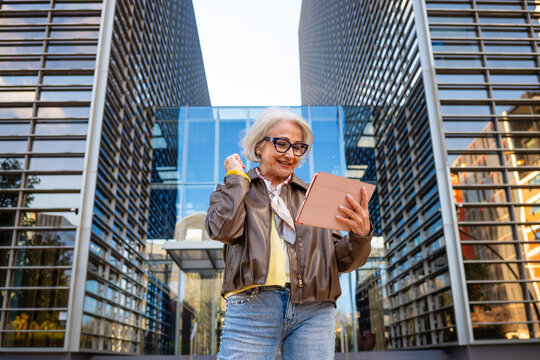 Senior woman celebrating success using a tablet in a business district