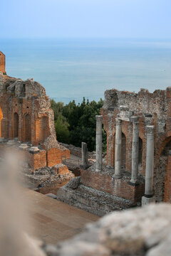 View of the ancient ruins of the Greek Theatre with stone columns and brick walls overlooking the Ionian Sea in Taormina, Sicily, Italy.