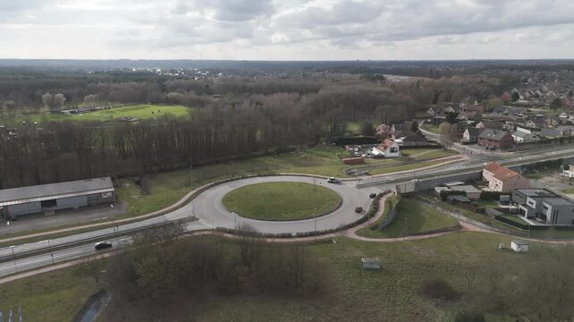 Genk, Belgium. Smooth lateral drone movement over suburban roundabout with surrounding residential landscape. Orbital drone flight.