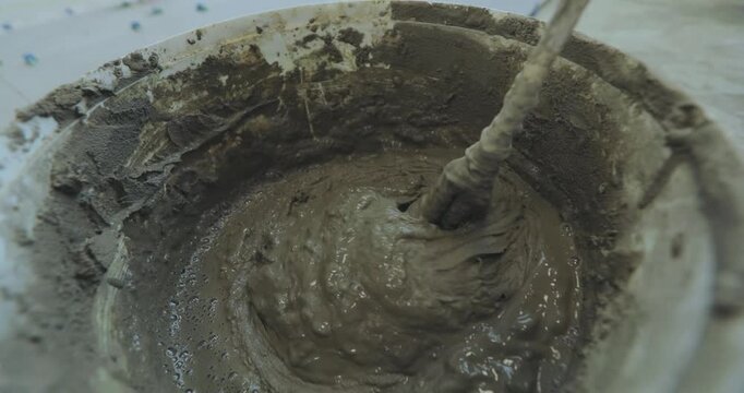 Mixing tile mortar for laying ceramic tiles or porcelain tiles. A man kneads tile mortar in a bucket with a paddle mixer or a paddle mixing drill. Close-up. Indoor. Inside