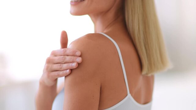 A woman with light skin smiles and poses with a tank top, revealing a small skin patch on her shoulder. The setting is bright and neutral, creating a welcoming environment.