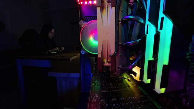 Zoom out. A man finishes working at his desk and places his legs on the table, captured in a wide-angle, close-up view from inside a gaming PC, highlighting the vibrant RGB lighting and hardware compo