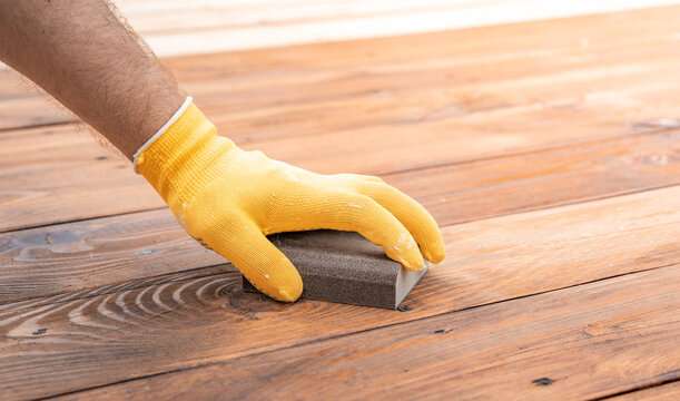 Hand in yellow glove sands wooden floorboards