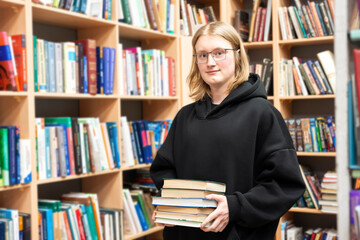 Young smiling man in a library with stack of books