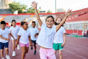 Fototapeta premium Young children having athletic exercise class running on the track, healthy lifestyle and children sport education concepts, finish line winner celebration, victory and success