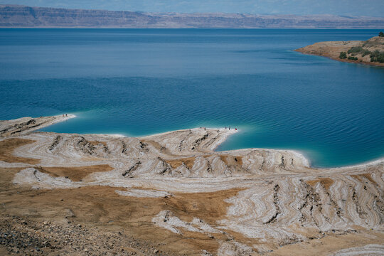 Turquoise waters and dramatic salt formations along the shoreline on the Jordanian side of the Dead Sea, showcasing a desert coastline landscape and natural patterns shaped by minerals and evaporation