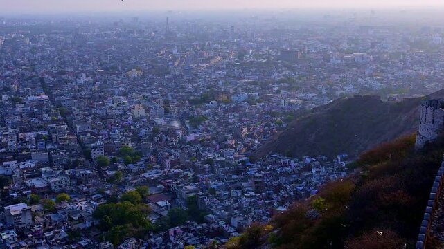 Evening view from Nahargarh Fort Jaipur showing fort wall and watch tower on Aravalli ridge with panoramic view of Jaipur city and buildings in sunset haze.