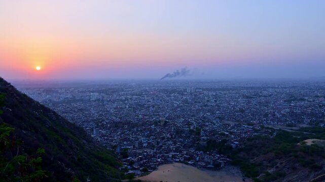 Sunset view from Nahargarh Fort Jaipur showing sun on horizon, Jaipur skyline, Aravalli hills, evening sky with orange-blue gradient and urban landscape.