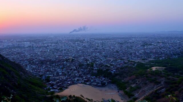 Sunset view from Nahargarh Fort Jaipur showing orange sun near horizon, wide Jaipur city view, Aravalli hills, evening sky gradient and skyline with smoke.