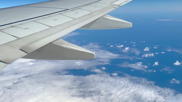 View from airplane window showing airplane wing flying above clouds at cruising altitude during commercial flight. Commercial aviation, air travel and transportation concept