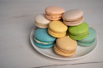 Obraz premium close-up of a stacked assortment of pastel macarons on a white plate, soft natural light revealing delicate shells and creamy fillings, set on a pale wooden table for an elegant inviting dessert