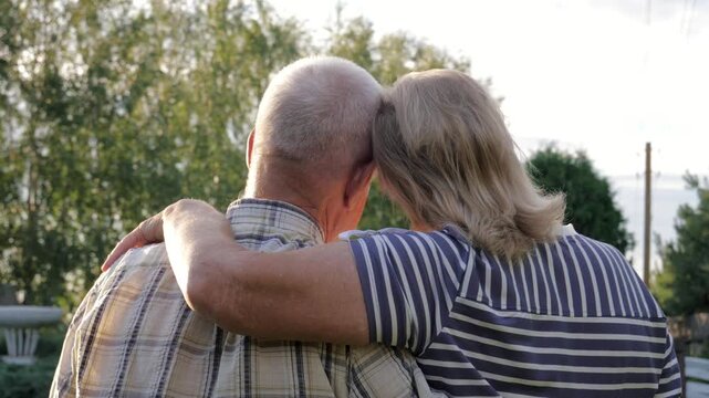Back view of elderly couple embracing affectionately in green park during warm sunset. Old peoples showcasing their lasting love, companionship and happy retirement life together. Family life