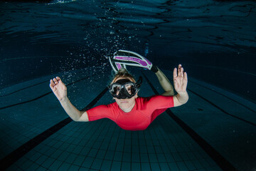 Woman swimming underwater in a dark blue swimming pool, wearing a red wetsuit, diving mask, and flippers © Zamrznuti tonovi