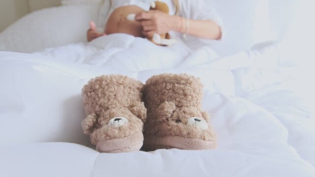 Pregnant woman relaxing in bed caressing her belly, with cute teddy bear baby shoes in front