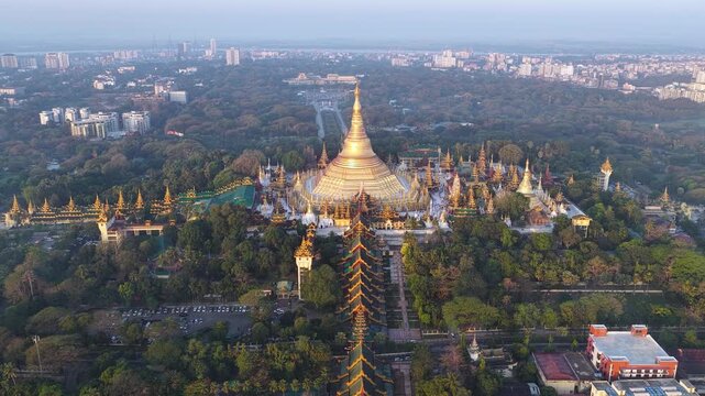 Aerial drone view at Shwedagon Pagoda, a golden stupa, surrounded by lush greenery and urban development in Yangon (Rangun), Myanmar (Burma), showcasing the city's blend of religious and modern life.