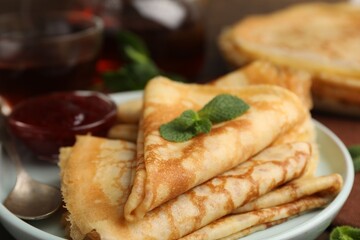 Tasty crepes with jam and mint leaves served on wooden table, closeup © New Africa