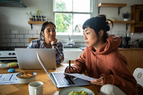 Two women budgeting with laptops at kitchen table
