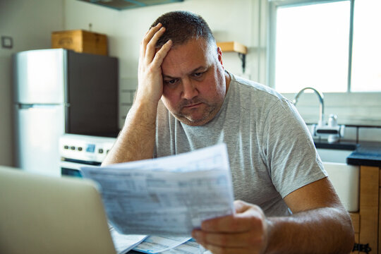 Concerned man reviewing household bills in home kitchen