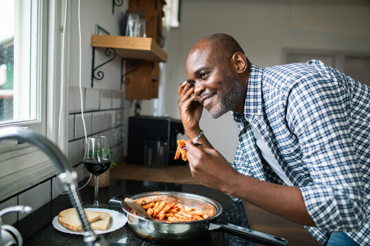 Smiling man tasting pasta in home kitchen