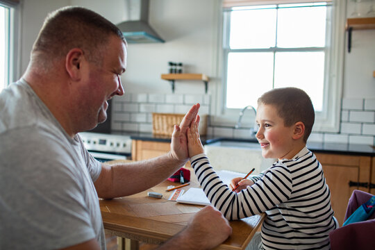 Father and son high five during homework in kitchen