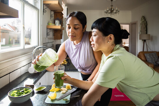 Two women making green smoothie in home kitchen