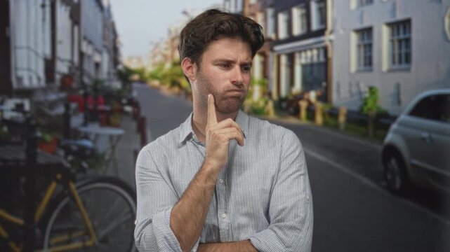 Man with hand on chin in pensive pose on a city street beside bicycle and parked car; thoughtful pondering doubt.
