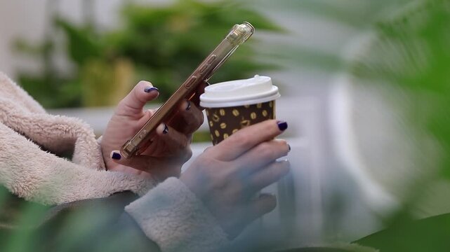 female hand holding mobile phone and coffee cup
