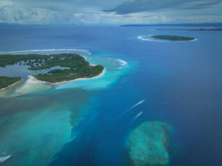 Obraz premium AERIAL: Reef with breaking waves, tropical island shoreline and deep blue Indian Ocean. Turquoise shallows, white sand and islands create a dramatic coastal scene. Surfing destination in Indonesia.