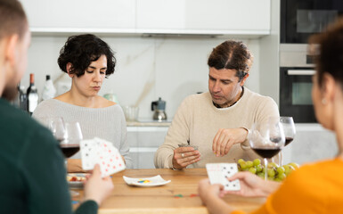 Fototapeta premium Happy group of friends playing poker cards and drinking wine at home