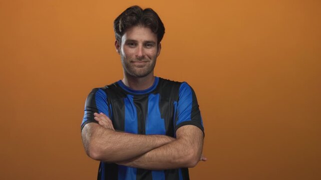 Man with crossed arms wearing blue and black soccer jersey bearing number 10 in orange studio; quiet confidence.