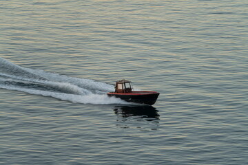 Fototapeta premium Small motorboat speeding across calm sea with wake