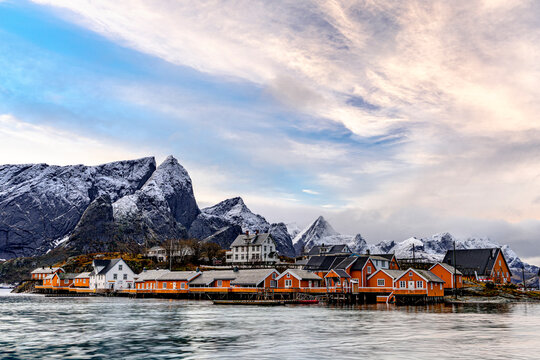 Fishing village with wooden houses near water and mountains in Lofoten Islands, Norway, during winter light