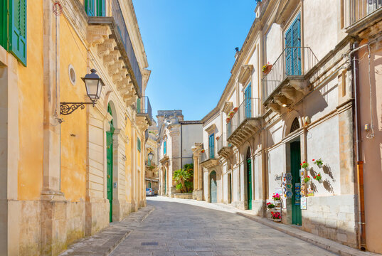 Narrow street in historic town of Ragusa Ibla with buildings and green shutters in Sicily Italy