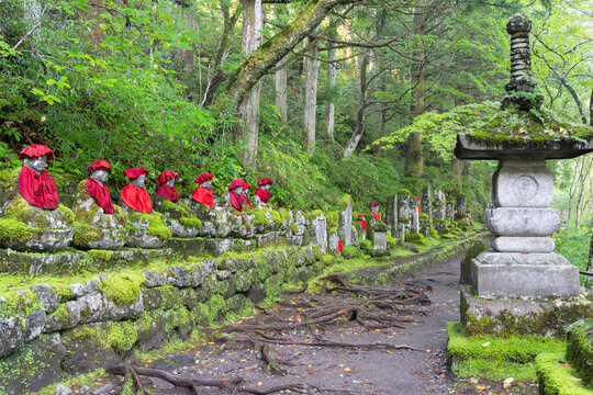 Stone jizo statues with red clothing along Kanmangafuchi Abyss under green trees in Nikko Tochigi Japan