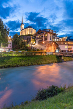 Church and river view in Kaprun at dusk with summer colors in the sky and lights in buildings