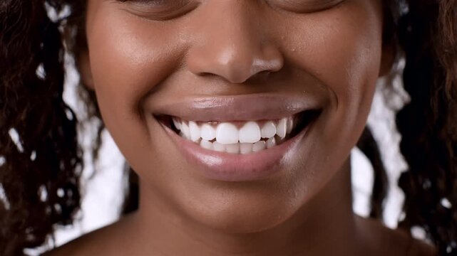 An African American woman smiles broadly, highlighting her teeth. Her natural hair frames her face against a light background. The setting feels inviting.
