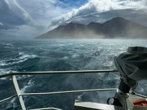 Gale force winds impact a ship in rough waters near rugged mountains in Tanaga Bay, Aleutian Islands, Alaska on a stormy day