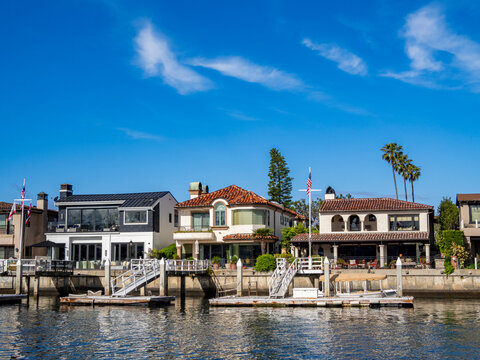 Multi million dollar homes line the water in Newport Beach with docks and clear blue skies above